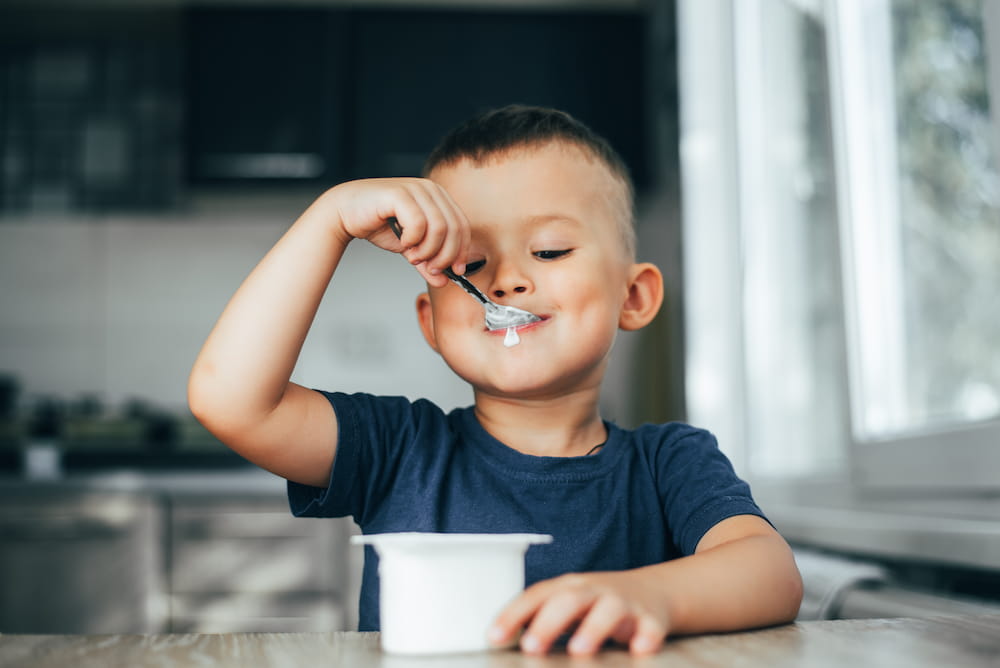 Young boy eats yogurt from plastic cup
