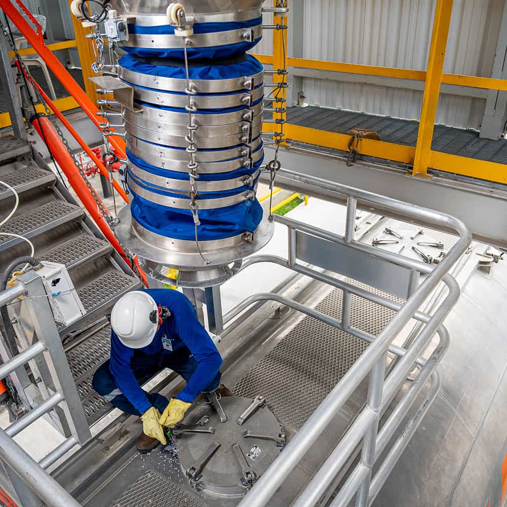 A man wearing a hard hat and gloves works on equipment