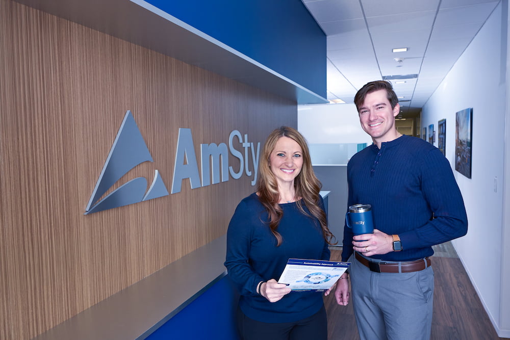 Man and woman pose in hallway of office looking at documents