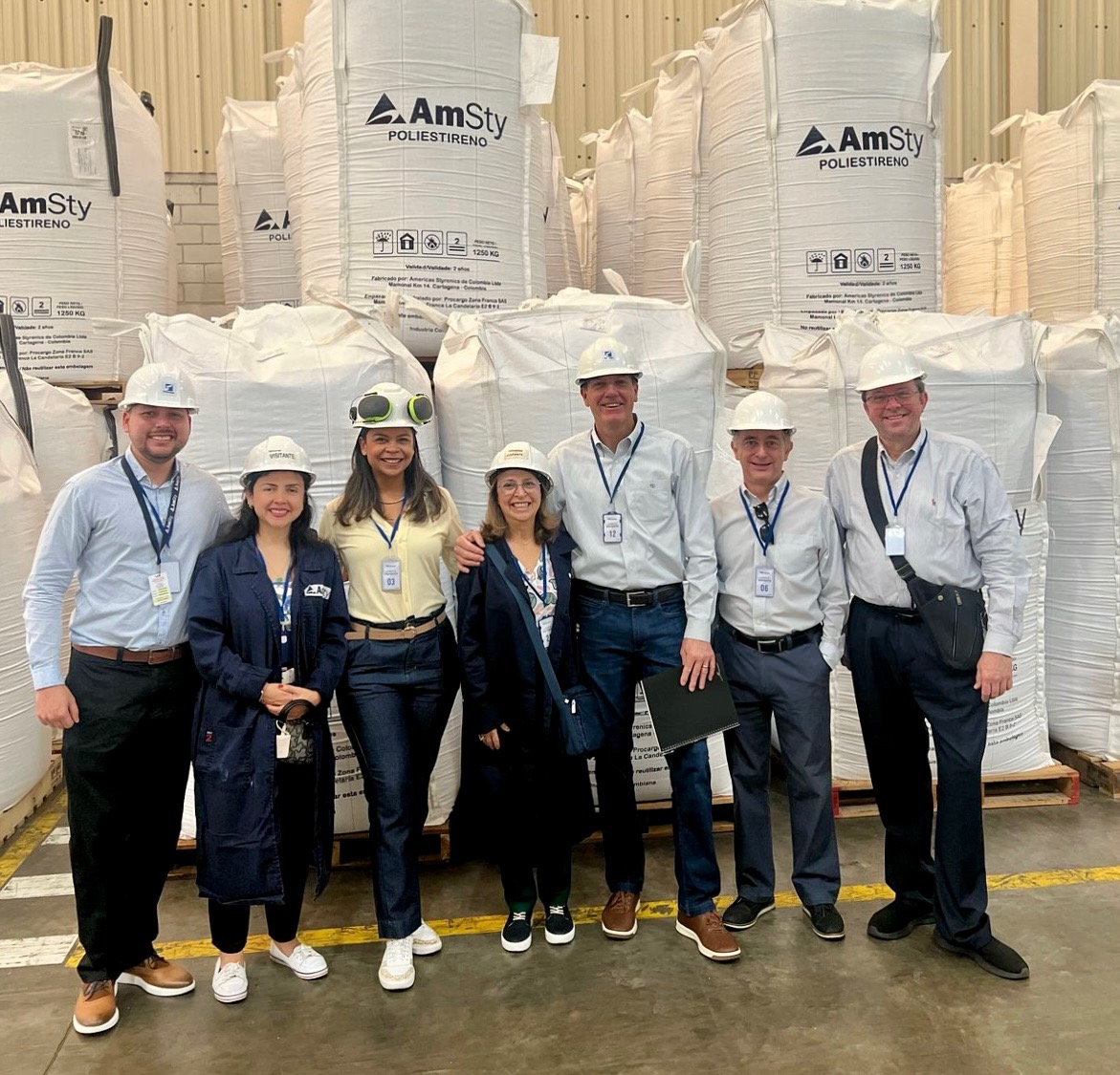 Men and women in hard hats pose in front of large bags stacked on pallets