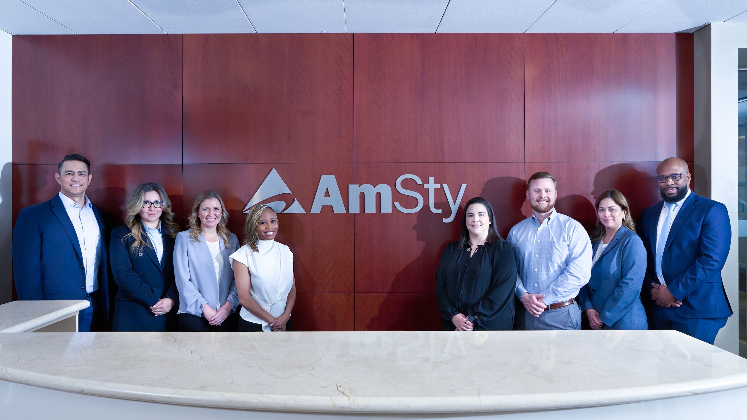 A group of employees stand in front of AmSty logo in office